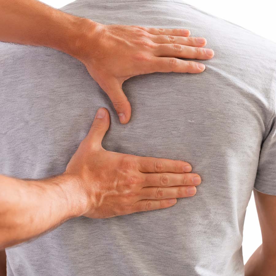 Two hands pressing on a person's upper back under a gray shirt, demonstrating a back massage technique